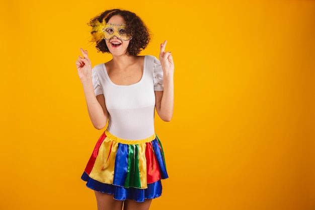Schöne Brasilianerin in Karnevalskleidung, buntem Rock und weißem Hemd, Daumen drücken und wünschen