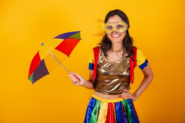 Schöne Brasilianerin in Karnevalskleidung mit Frevo-Kleidung und buntem Regenschirm und Maske