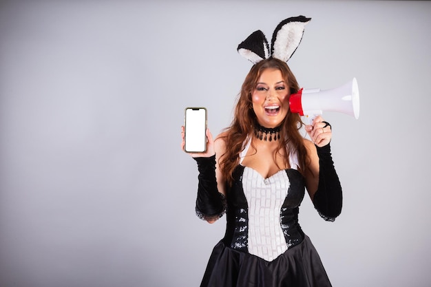 Schöne Brasilianerin mit Hasenkleidung Ostern mit Smartphone neben mobiler Megaphon-App-Werbung