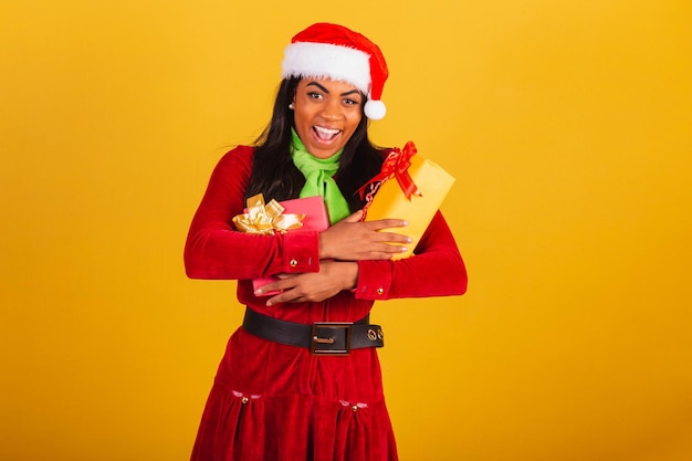 Schöne brasilianische schwarze Frau, gekleidet in Weihnachtskleidung Weihnachtsmann umarmt zwei Geschenke