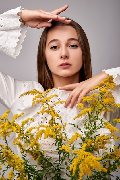 Schöne braunhaarige Frau mit gelben Mimosenblumen auf einem weißen Hintergrund. Frühlingsporträt eines Mädchens