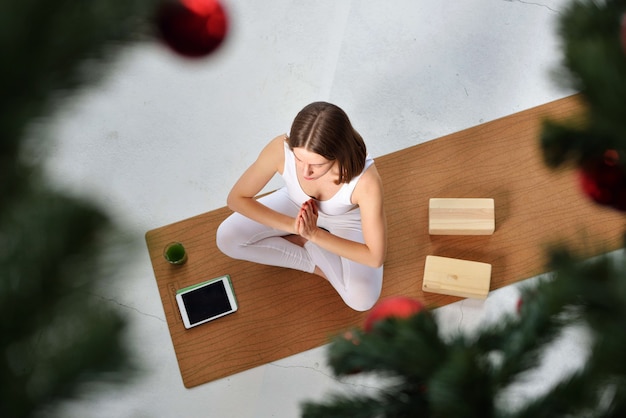 Schöne braunhaarige junge Frau mit weißer Sportkleidung, die zu Weihnachten Yoga praktiziert, Heimsportkonzept. v Konzept des gesunden Lebensstils Draufsicht. Platz für Text.