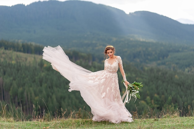 Schöne Braut, die in ihrem Hochzeitskleid auf einem Hintergrund der Berge aufwirft.