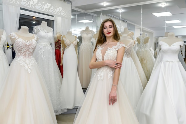 Schöne Braut im Hochzeitskleid, das in der Boutique steht