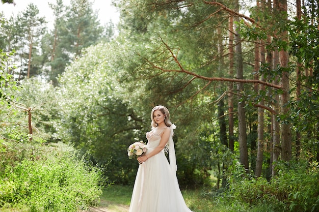 Schöne Braut im Luxushochzeitskleid, das Blumenstrauß beim Gehen im Park hält