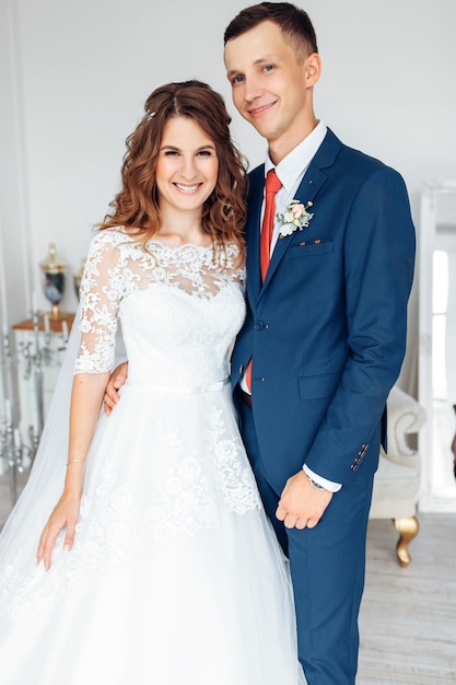 Schöne Braut im weißen Kleid und im Bräutigam im Anzug, posierend im weißen Studio-Interieur, Hochzeit