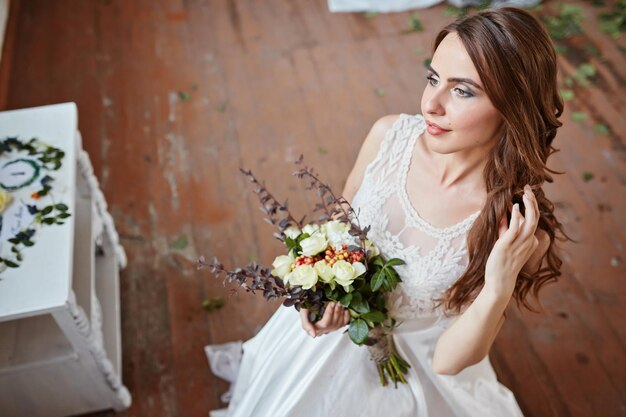 Schöne Braut in einem Hochzeitskleid in einem hellen, stilvollen Studio Hochzeit im europäischen Stil Dekor und Blumenstrauß in der Hand