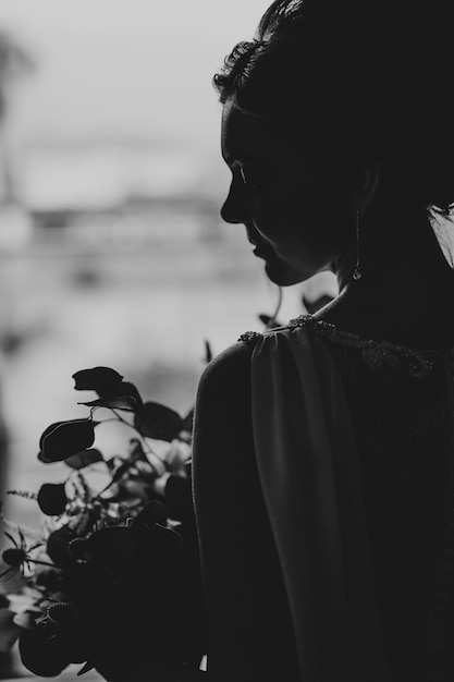 Schöne Braut in einem Spitzenkleid mit einem Blumenstrauß im Zimmerporträt schwarz-weiß Foto