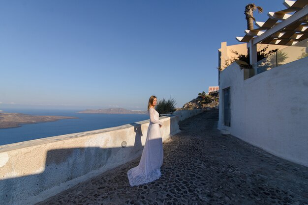 Schöne Braut In einem weißen Kleid, das vor dem Hintergrund des Mittelmeers in Thira, Santorini aufwirft.