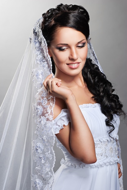 Schöne Braut steht im Hochzeitskleid auf grauem Hintergrund