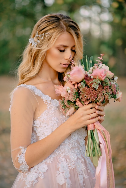 Schöne Braut steht mit einem Blumenstrauß in den Händen auf einem Naturhintergrund