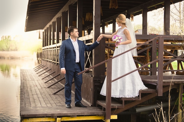 Schöne Braut und hübscher Bräutigam, die die Treppe am Pier hinuntergehen down