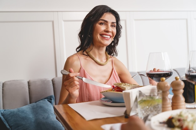 Schöne brünette Dame, die mit leckerem Essen am Tisch sitzt und lächelt