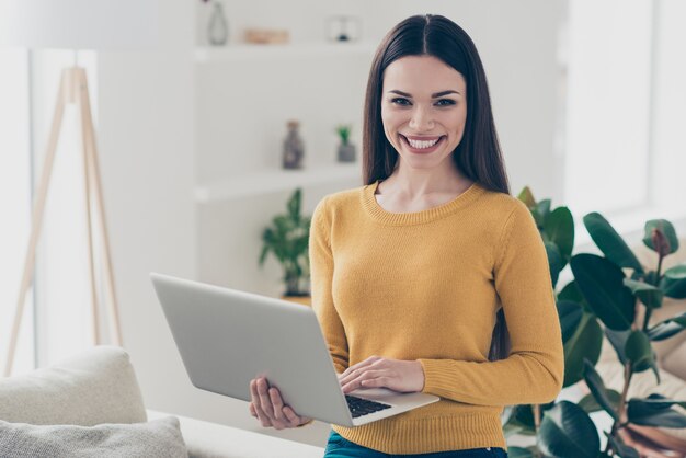 Schöne brünette Frau, die drinnen mit ihrem Laptop aufwirft