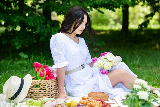 schöne brünette Frau, die im Park auf einer Picknickdecke sitzt und sich in der Natur ausruht