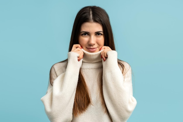 Schöne brünette Frau mit beigem Rollkragenpullover über blauem Hintergrund glückliches Gesicht lächelnd in die Kamera schauen Positives Personenkonzept