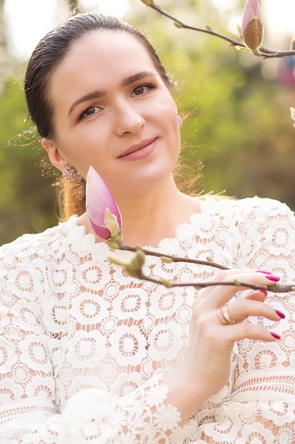 Schöne brünette Frau mit natürlichem Make-up, die in der Nähe der blühenden Magnolienblumen posiert