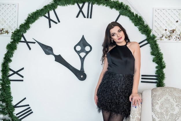 Schöne Brünette im schwarzen Kleid, das mit Uhr aufwirft