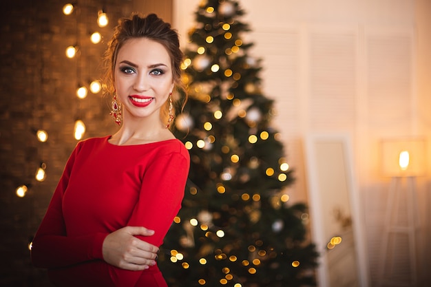Schöne Brünette in einem roten Kleid auf dem Hintergrund des Weihnachtsbaums.