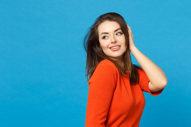 Schöne brünette junge Frau in rot-orangefarbenem Kleid, die zur Seite schaut und isoliert über trendigem blauem Wandhintergrund posiert, Studioporträt. Lifestyle-Modekonzept für Menschen. Mock-up-Kopienbereich.