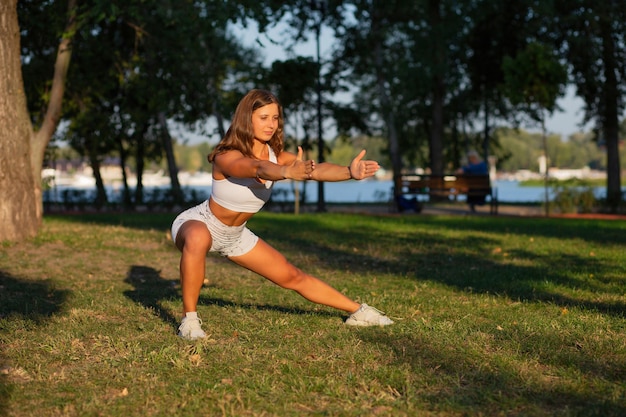 Schöne brünette junge Frau mit athletischer Figur, die Pilates macht und im Park trainiert