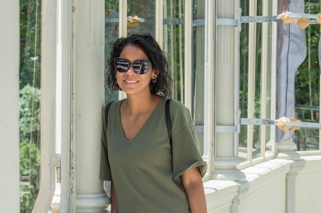 Schöne brünette Latinerin mit grünem Hemd und Sonnenbrille in der Nähe des Fensters