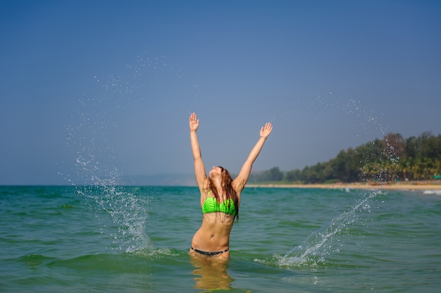 Schöne Brünette mit langen Haaren steht im Meer und hebt ihre Hände und ihr Gesicht zur Sonne und zum Himmel