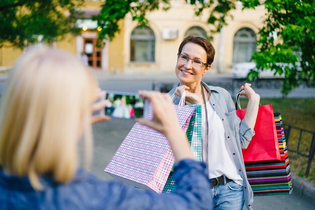 Foto schöne brünette posiert für smartphone-kamera mit einkaufstüten auf der straße