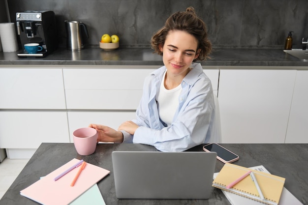 Schöne brünette Studentin studiert Online-Kurs von zu Hause aus. Tutorin arbeitet auf Fernbedienung und schaut auf