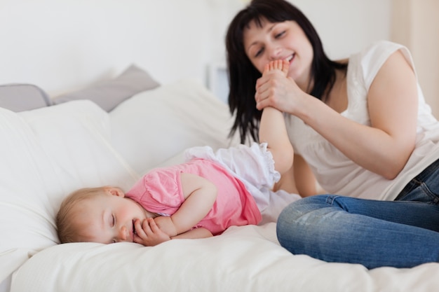 Schöne Brunettefrau, die mit ihrem Baby beim Lügen auf einem Bett spielt