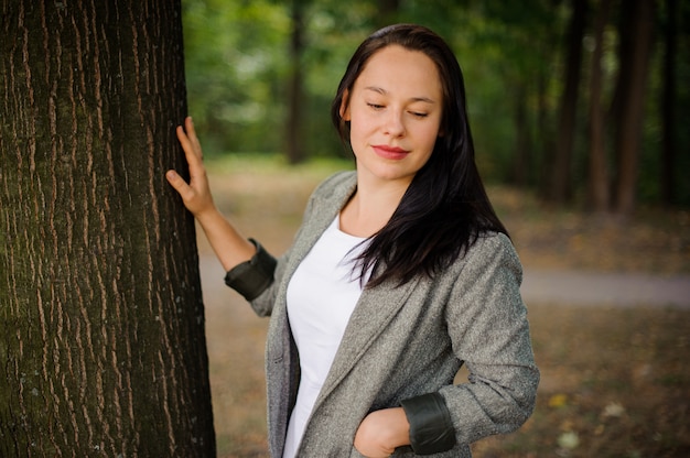 Schöne Brunettefrau, die nahe dem Baum steht