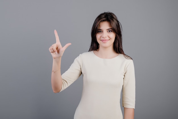 Schöne Brunettefrau, die zwei Finger getrennt über Grau zeigt