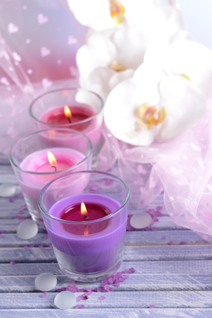 Schöne bunte Kerzen und Orchideenblumen auf farbigem Holztisch auf hellem Hintergrund