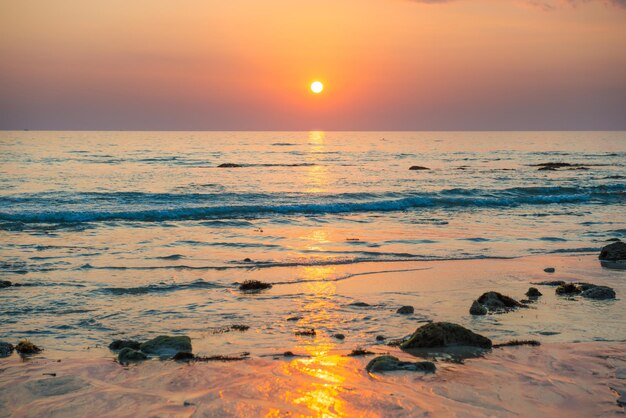 Schöne bunte Sonnenunterganglandschaft mit Sandstrand, goldener Sonne und Steinen am Meeresufer