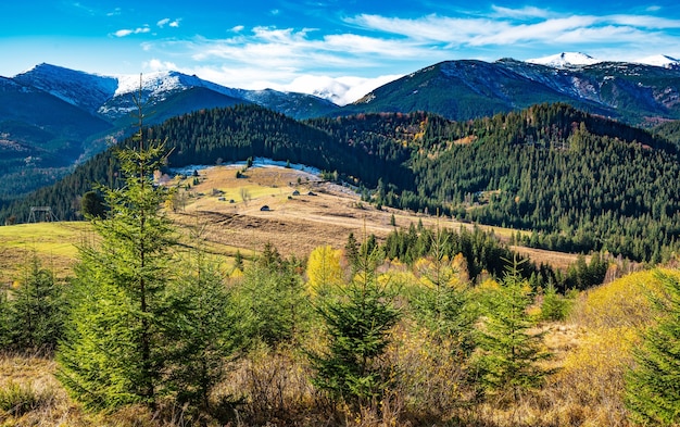 Schöne bunte Wälder, die die Karpaten bedecken, und ein kleines Dorf vor dem Hintergrund eines warmen Herbsthimmels