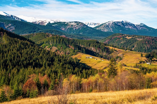 Schöne bunte Wälder, die die Karpaten bedecken, und ein kleines Dorf vor dem Hintergrund eines warmen Herbsthimmels