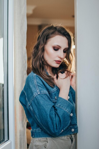 Schöne charmante Frau mit welligem Haar und professionellem Make-up in einer Jeansjacke und kurzen Top-Posen