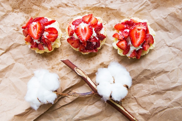 Schöne Cupcakes mit Erdbeeren und einem Baumwollzweig liegen auf Kraftpapier