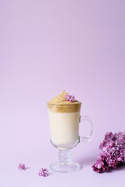 Schöne Dalgona trinken einen schaumigen Kaffee in einer transparenten Tasse und blüht lila zu lila Il lila Hintergrund. Neben der Tasse ist ein Marshmallow und ein Fliederzweig.