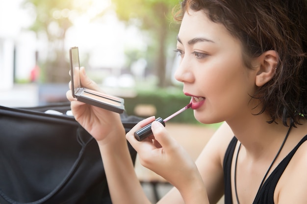 schöne Dame benutzen Lippenstift, um ihr Gesicht mit Spiegel zu machen