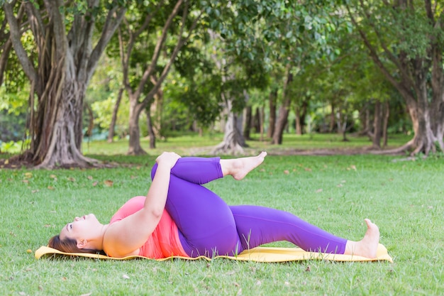 Schöne dicke Frau, die Yoga auf der Matte im Park tut