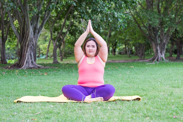 Schöne dicke Frau, die Yoga auf der Matte im Park tut