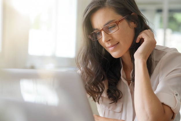 Schöne dunkelhaarige Frau mit den Gläsern, die an Laptop arbeiten