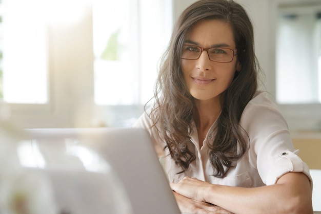 Schöne dunkelhaarige Frau mit den Gläsern, die an Laptop arbeiten