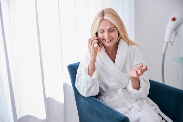 Schöne elegante Frau, die sich auf dem Handy unterhält, während sie Zeit im Schönheitszentrum verbringt?