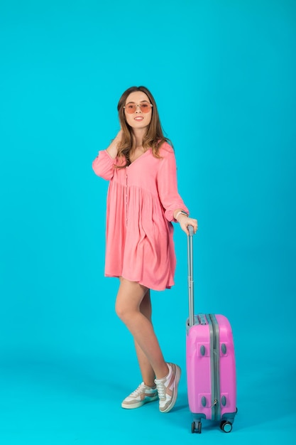 Schöne elegante Frau in einem rosa Kleid mit einem rosa großen Koffer für die Reise