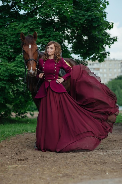Schöne elegante Frau in langem, fließendem Kleid und reinrassigem braunem Pferd. Spaziergang mit Pferd im Wald