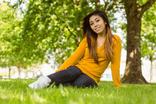 Schöne entspannte Frau, die auf Gras am Park sitzt