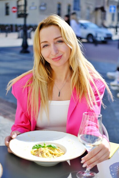 Schöne erwachsene blonde Frau sitzt auf einer Sommerterrasse in einem Café Die Frau isst Nudeln