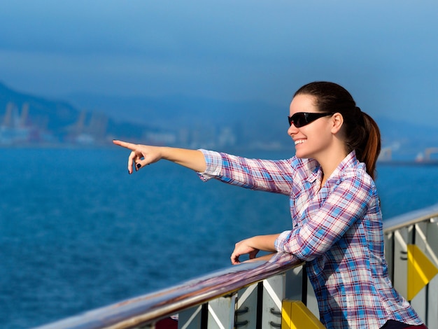 Schöne erwachsene Frau, die auf dem Deck eines Kreuzfahrtschiffes steht und auf etwas zeigt